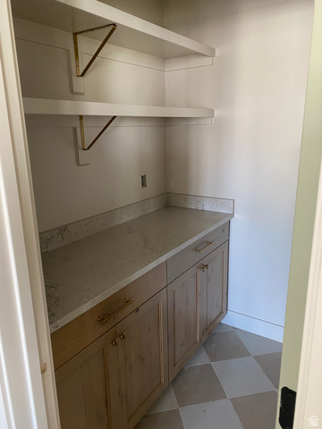 4676 West 75 North, Unit 401 West Point, UT 84015 - Photo 5 of 17 Pantry featuring floating white shelving with brass brackets, light wood-finish cabinetry, light-toned countertop, and checkered tile flooring