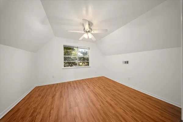 an empty room with wooden floor chandelier fan and windows