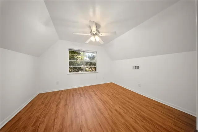 an empty room with wooden floor chandelier fan and windows