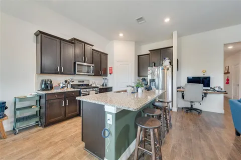 a open kitchen with stainless steel appliances granite countertop a stove a sink a dining table and chairs with wooden floor