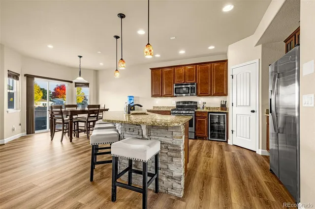 a kitchen with stainless steel appliances granite countertop a refrigerator a stove top oven a sink dishwasher and a dining table with wooden floor