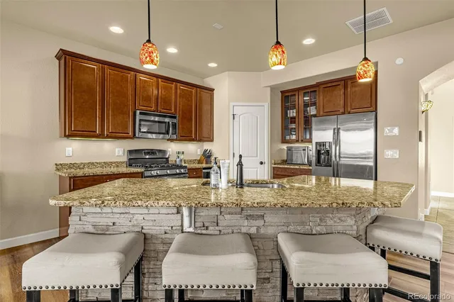 a kitchen with stainless steel appliances granite countertop a stove top oven a sink a dining table and chairs with wooden floor