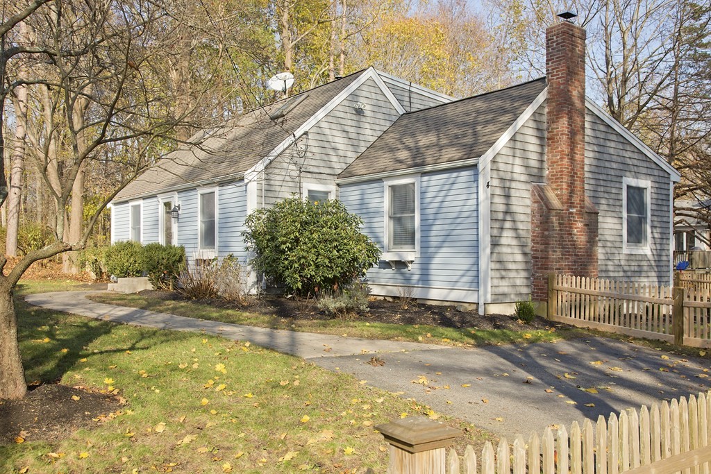 a view of yellow house with small yard plants and large tree