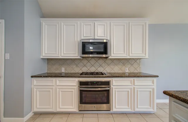 a large kitchen with granite countertop a white cabinets and chandelier