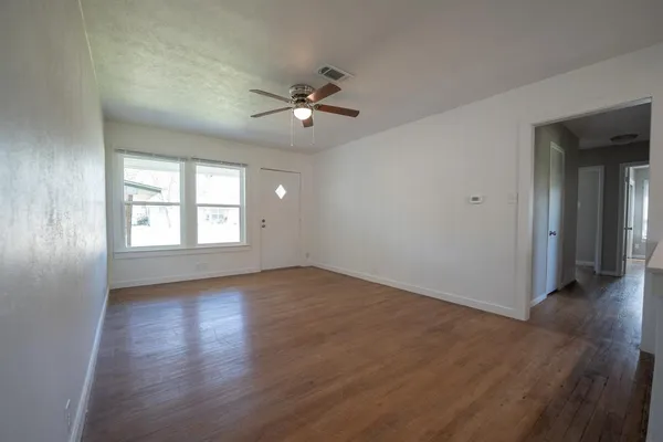 an empty room with wooden floor chandelier fan and windows