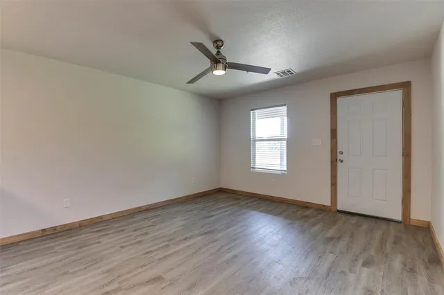 an empty room with wooden floor ceiling fan and windows