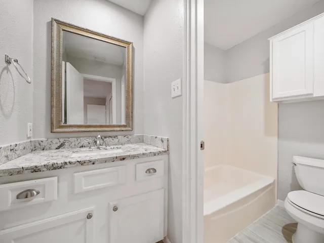 a bathroom with a granite countertop toilet a sink and a mirror