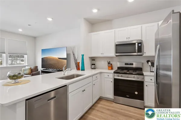 a kitchen with stainless steel appliances a sink dishwasher a refrigerator a stove a microwave oven with cabinets and wooden floor