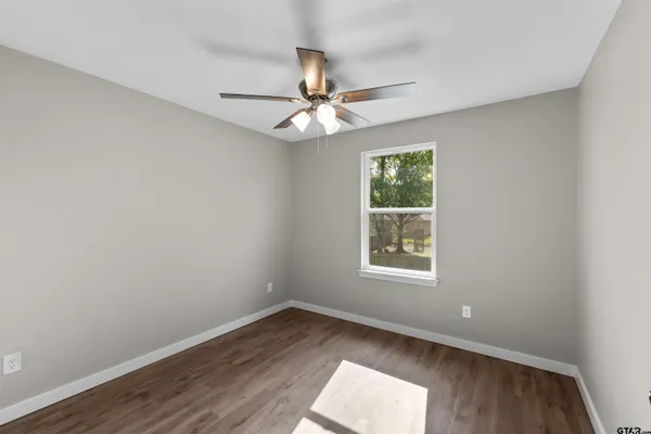 an empty room with wooden floor ceiling fan and windows