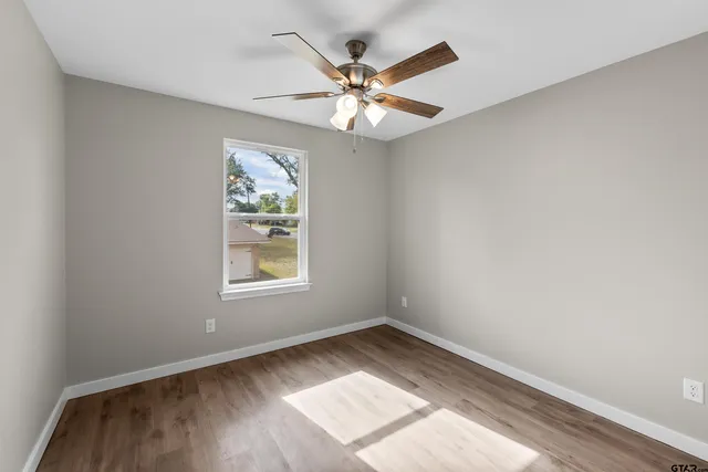 an empty room with wooden floor fan and windows