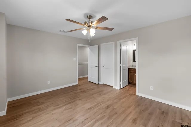 a view of an empty room with wooden floor and a ceiling fan
