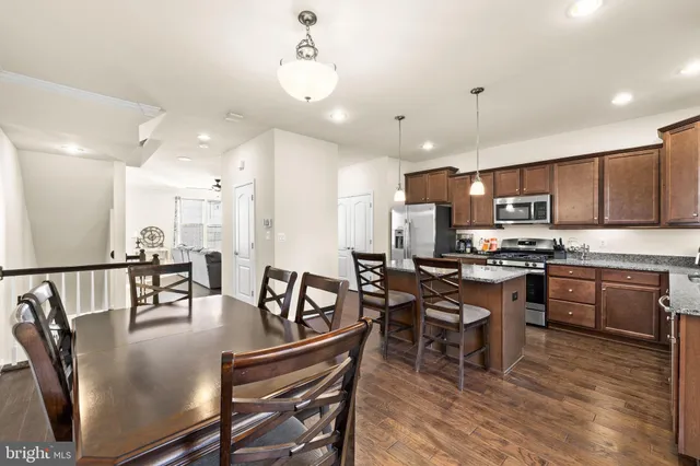 a kitchen with stainless steel appliances granite countertop a stove a refrigerator a kitchen island a dining table and chairs with wooden floor