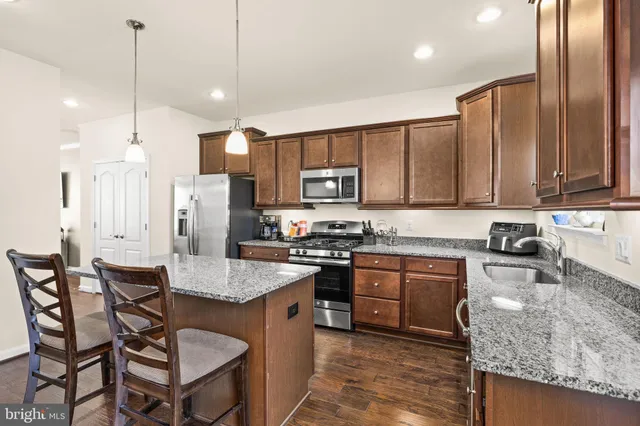 a kitchen with stainless steel appliances granite countertop a stove top oven a refrigerator a sink and chairs