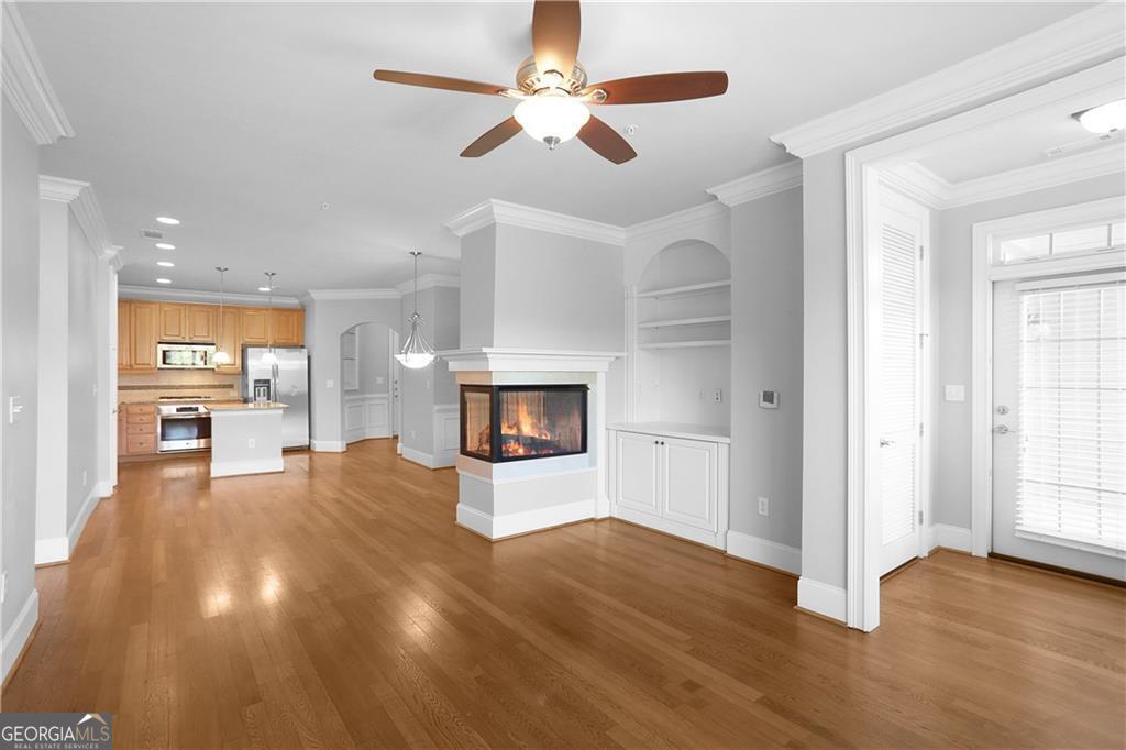 an empty room with wooden floor a ceiling fan and kitchen view