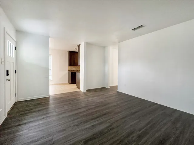 a view of empty room with wooden floor and kitchen