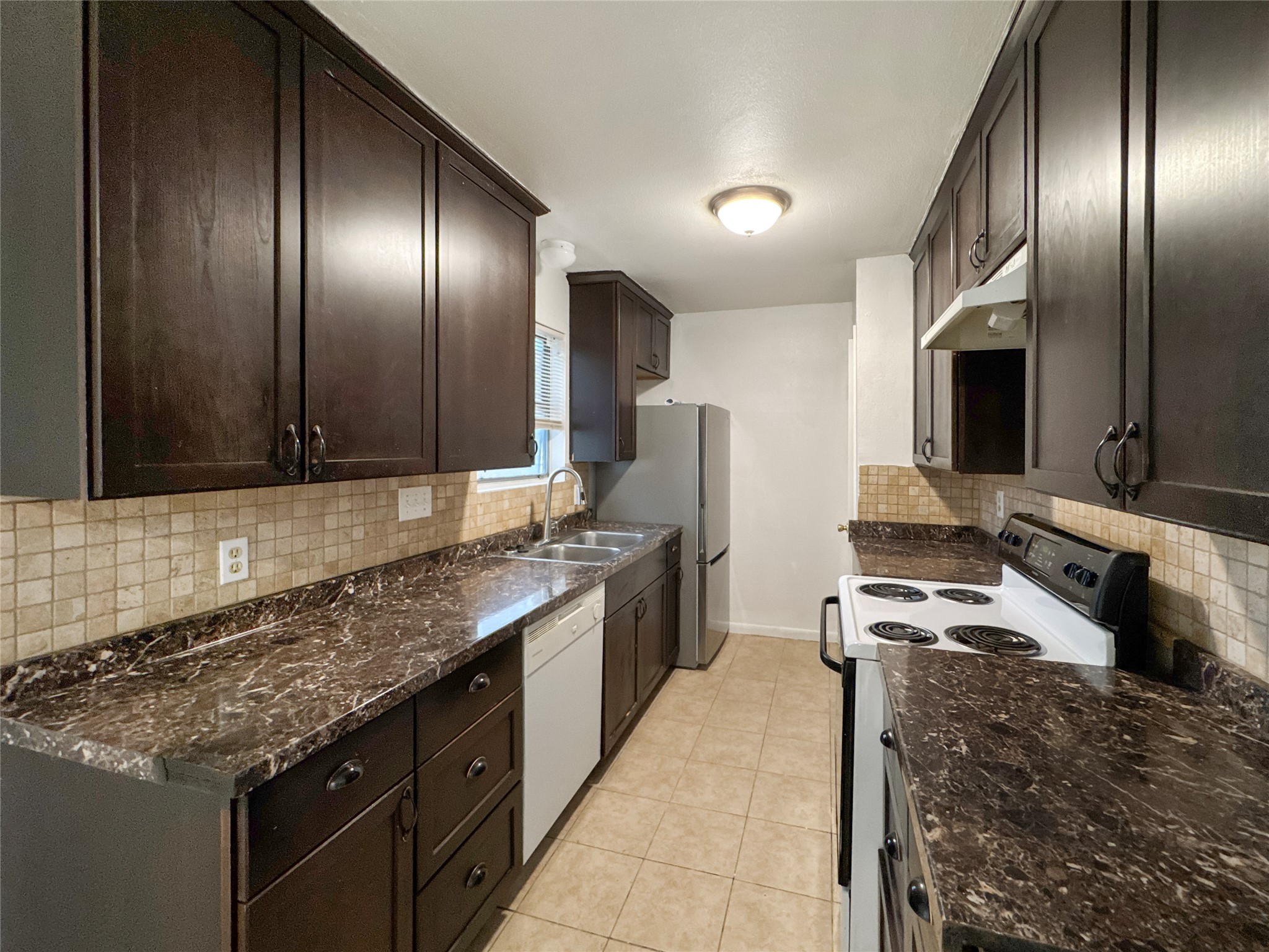 2017 Greenbrook Parkway, Unit B Austin, TX 78723 - Photo 5 of 14 Kitchen with white appliances, dark brown cabinets, under cabinet range hood, decorative backsplash, and dark stone counters
