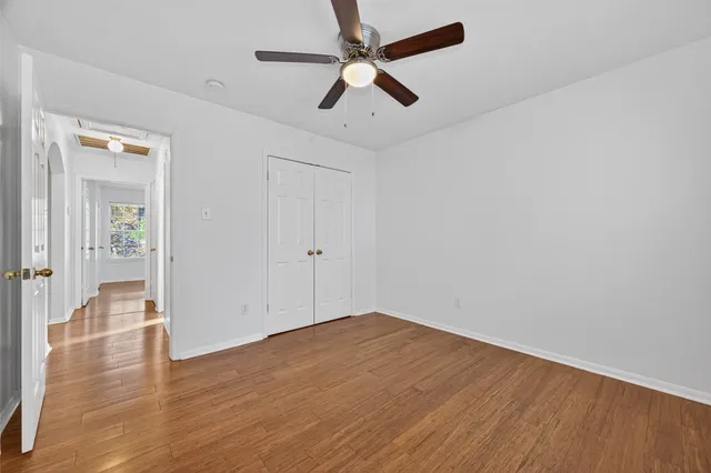 an empty room with wooden floor ceiling fan and windows