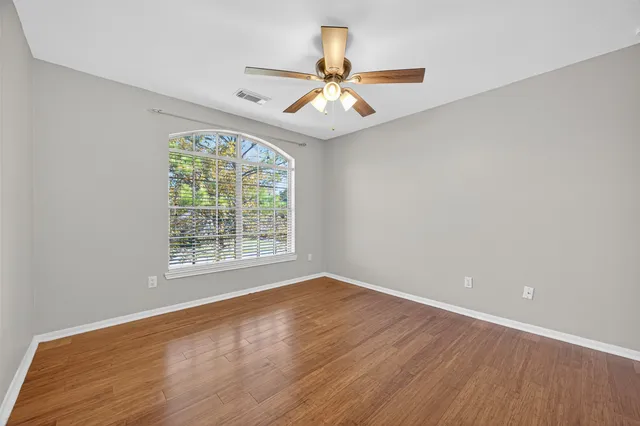 an empty room with wooden floor chandelier fan and windows