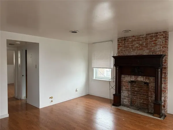 an empty room with wooden floor fireplace and windows