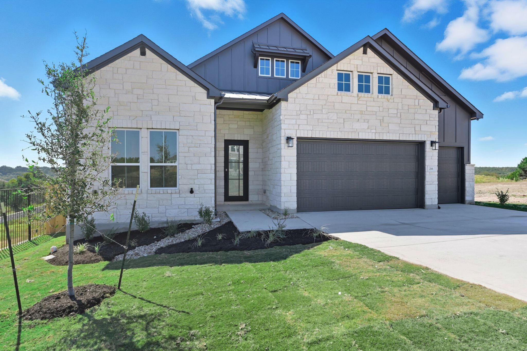 View of front of house featuring board and batten siding, stone siding, a garage, driveway, and a metal roof