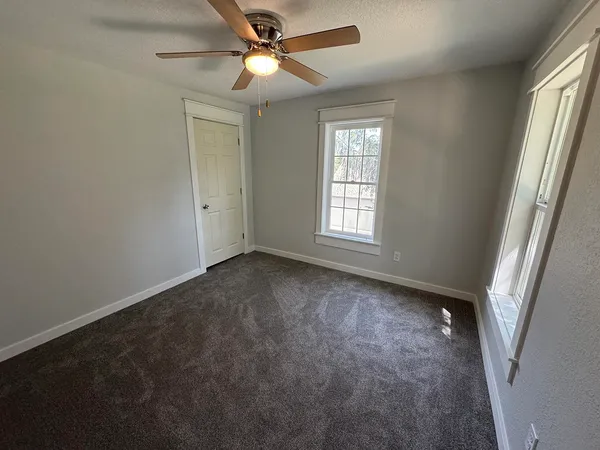an empty room with a chandelier fan and windows