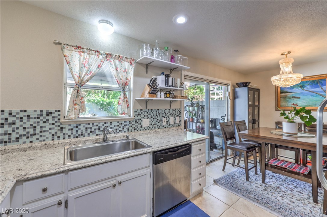 8056 Cimarron Ridge Drive, Unit 101 Las Vegas, NV 89128 - Photo 12 of 31 Kitchen with stainless steel dishwasher, tasteful backsplash, light tile patterned floors, white cabinetry, and a chandelier