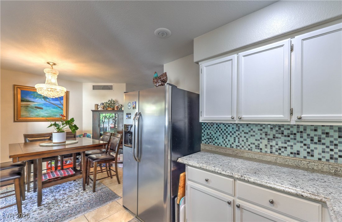 8056 Cimarron Ridge Drive, Unit 101 Las Vegas, NV 89128 - Photo 13 of 31 Kitchen with stainless steel refrigerator with ice dispenser, white cabinetry, decorative backsplash, light tile patterned floors, and hanging light fixtures