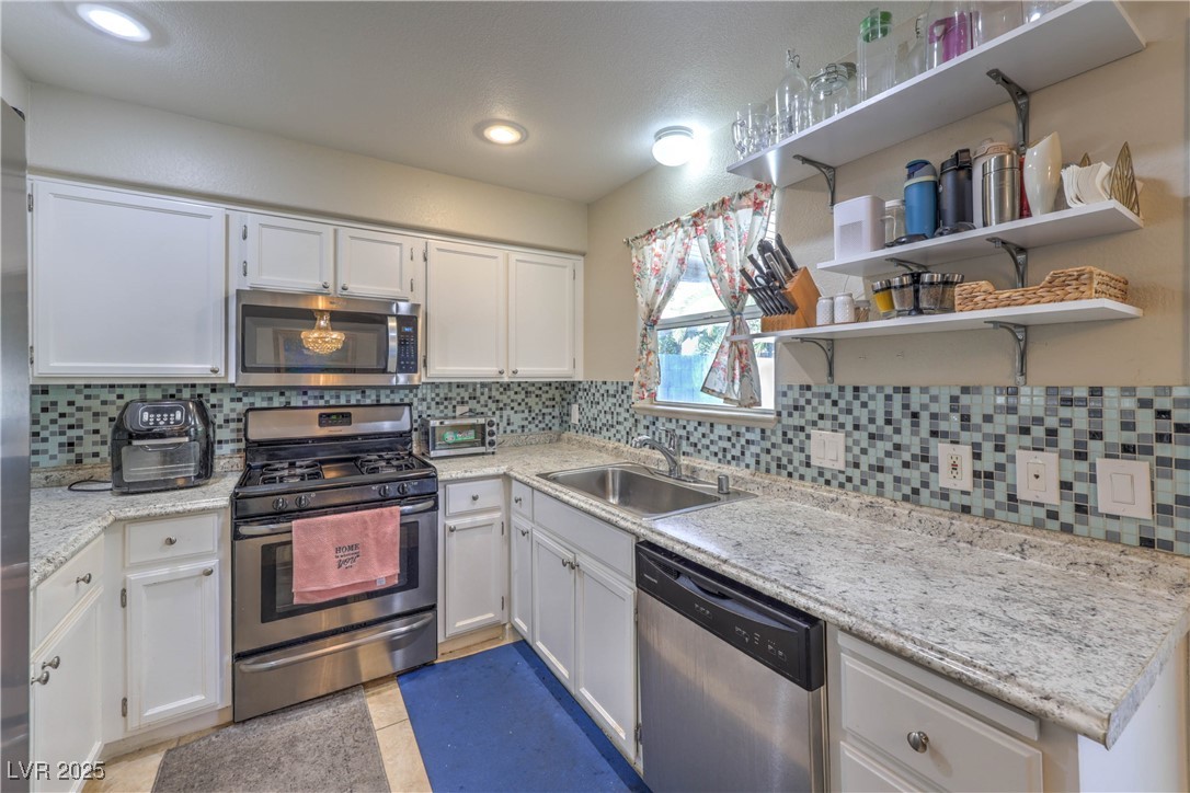 8056 Cimarron Ridge Drive, Unit 101 Las Vegas, NV 89128 - Photo 10 of 31 Kitchen with appliances with stainless steel finishes, white cabinetry, backsplash, light tile patterned floors, and open shelves