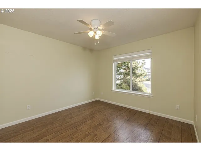 an empty room with wooden floor chandelier fan and windows