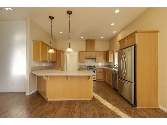 a kitchen with stainless steel appliances granite countertop a refrigerator a sink dishwasher a stove and a dining table with wooden floor