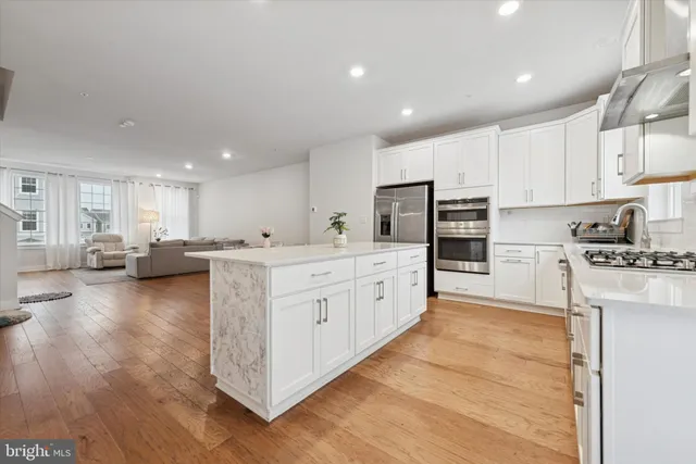 a kitchen with stainless steel appliances kitchen island granite countertop a stove a sink a refrigerator and white cabinets with wooden floor