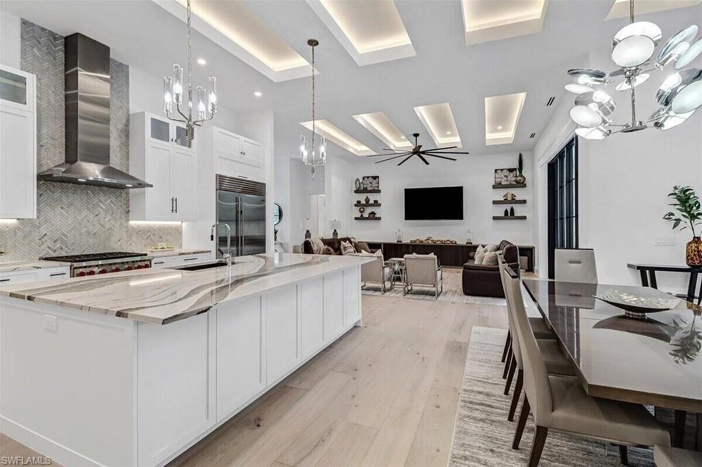 1546 Mandarin Road Naples, FL 34102 - Photo 17 of 48 Kitchen featuring wall chimney exhaust hood, a large island with sink, appliances with stainless steel finishes, and white cabinets