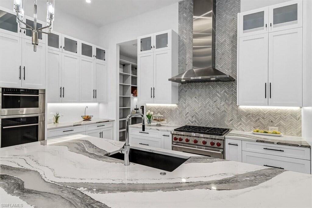 1546 Mandarin Road Naples, FL 34102 - Photo 18 of 48 Kitchen featuring wall chimney range hood, stainless steel appliances, light stone counters, and pendant lighting