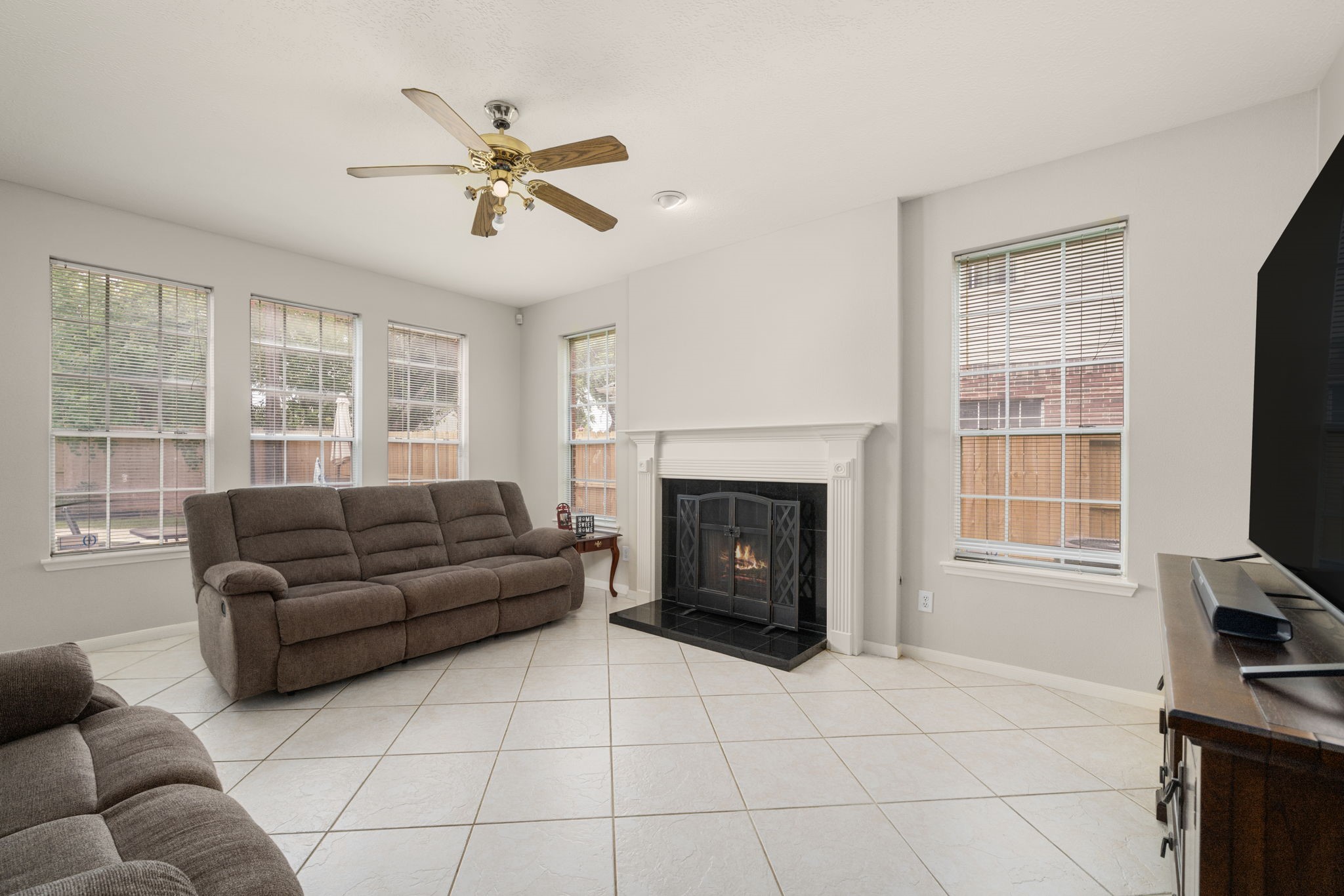 9715 Therrell Drive Houston, TX 77064 - Photo 13 of 33 Cozy and bright family room with large windows, a central fireplace, and tile flooring.