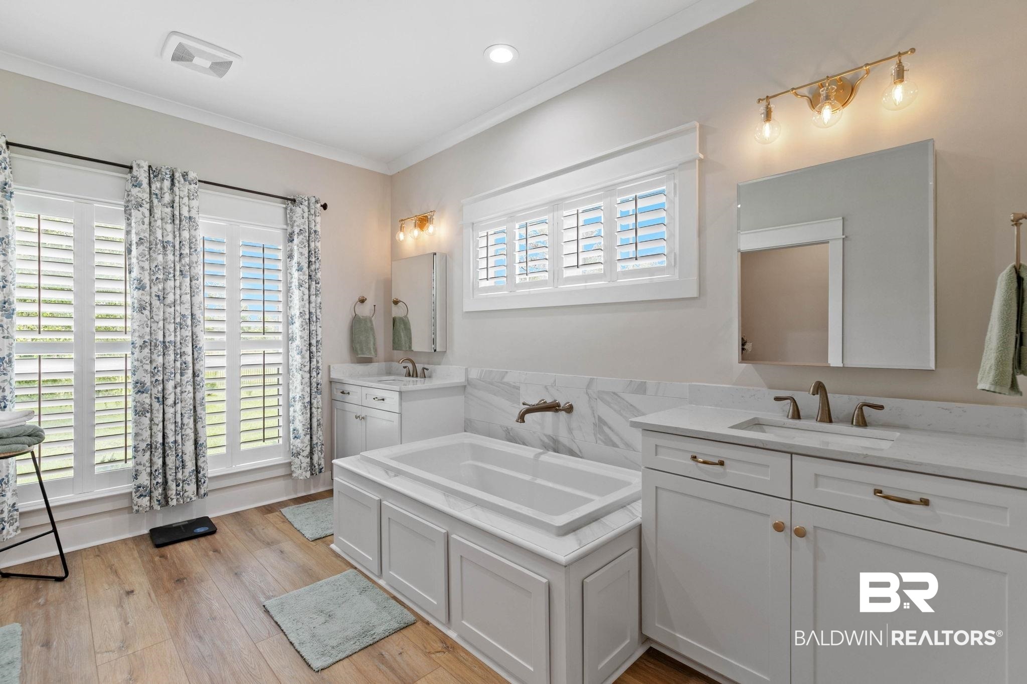 2029 George Lee Road Repton, AL 36475 - Photo 27 of 58 Contemporary bathroom featuring an integrated soaking tub with a surrounding marble-look tile, dual vanities with white shaker cabinetry, and wood-finish flooring