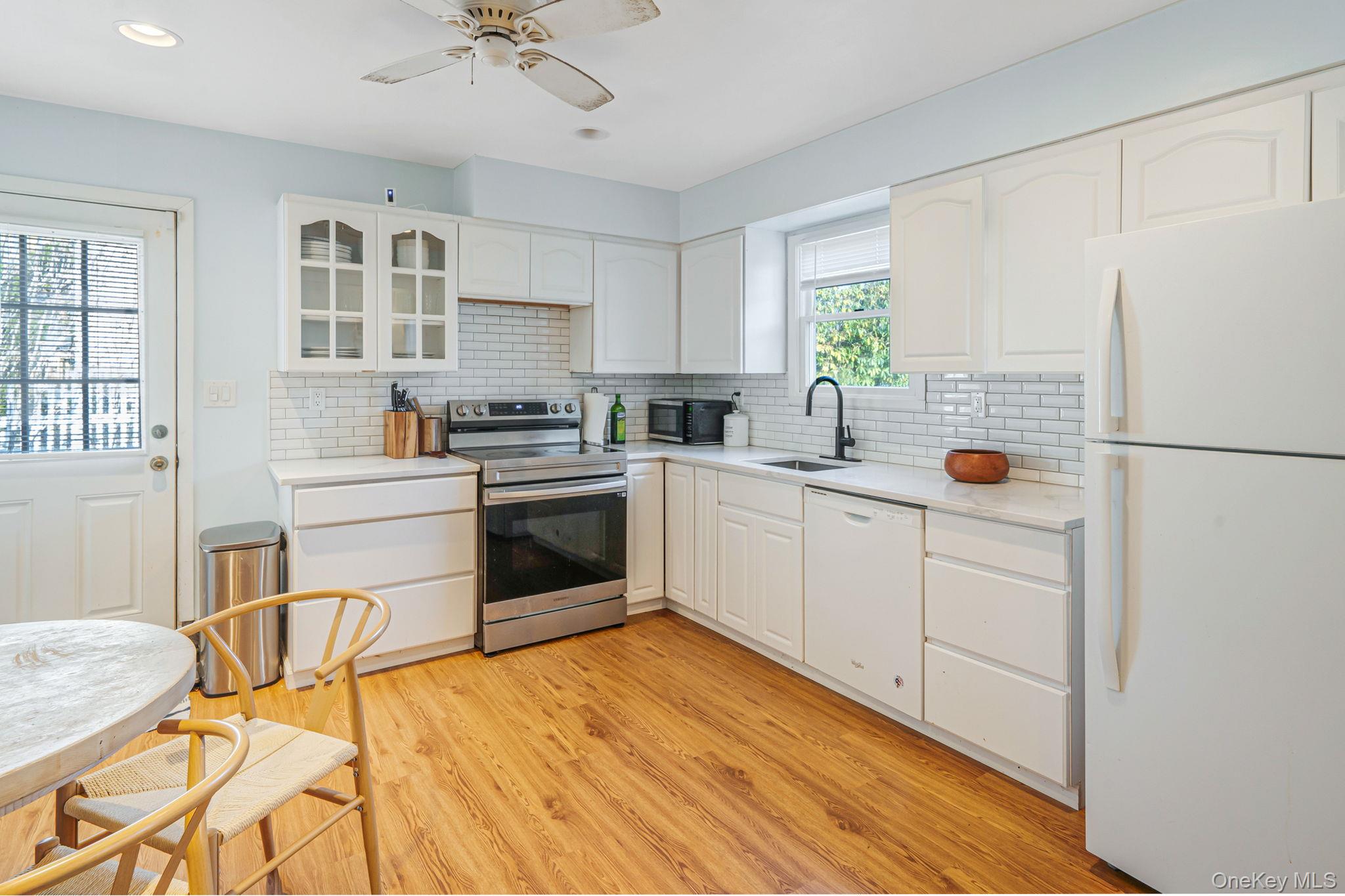 39 Kay Road Calverton, NY 11933 - Photo 6 of 17 Kitchen with white appliances, glass insert cabinets, white cabinetry, light wood-style floors, and backsplash
