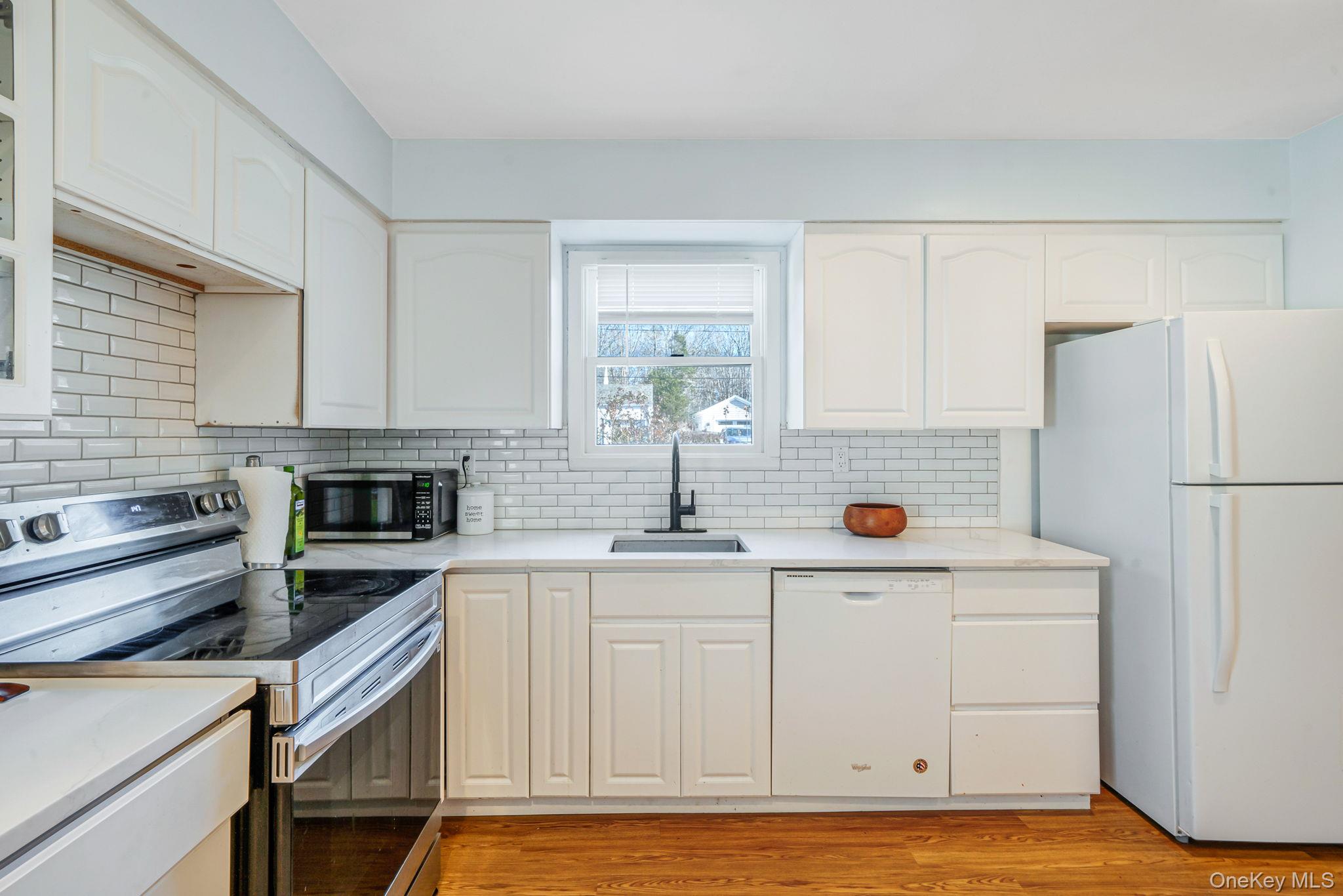 39 Kay Road Calverton, NY 11933 - Photo 8 of 17 Kitchen featuring white appliances, white cabinets, light wood-style floors, and tasteful backsplash