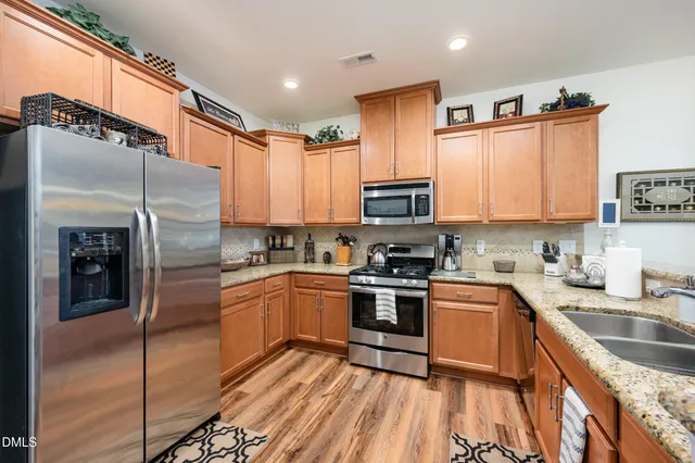 a kitchen with stainless steel appliances granite countertop a refrigerator a sink dishwasher a stove with wooden cabinets and floor