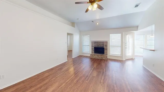 an empty room with wooden floor fireplace and windows