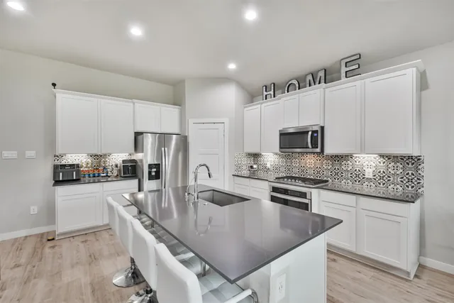 a kitchen with stainless steel appliances granite countertop a stove a sink a microwave a refrigerator white cabinets and wooden floor