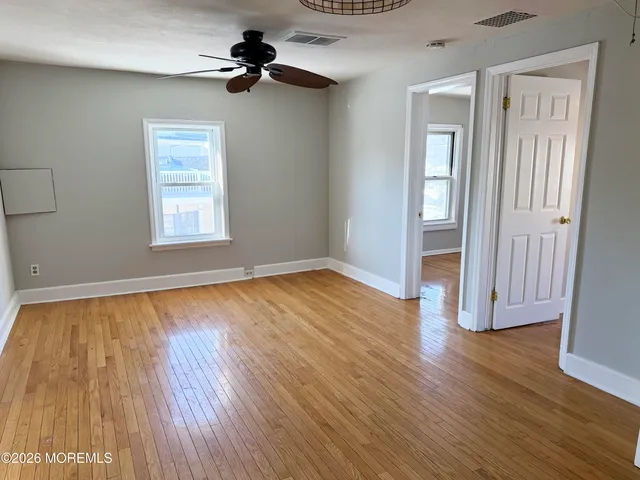 an empty room with wooden floor chandelier fan and windows