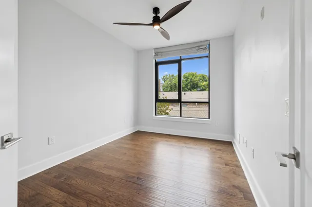 an empty room with wooden floor ceiling fan and windows