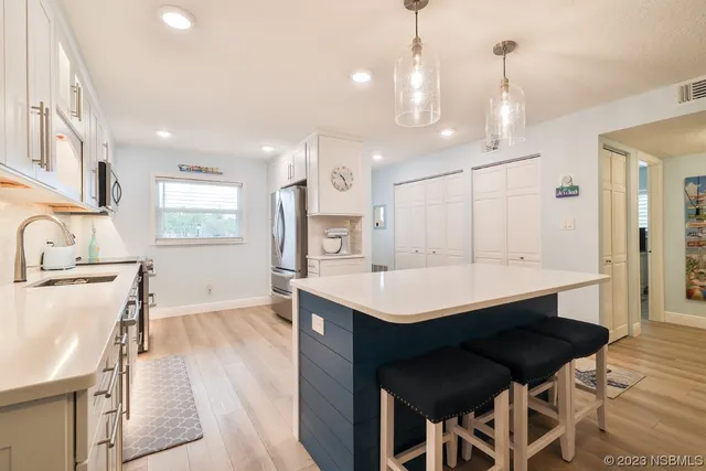 a large white kitchen with a large island in the center a sink a window and stainless steel appliances