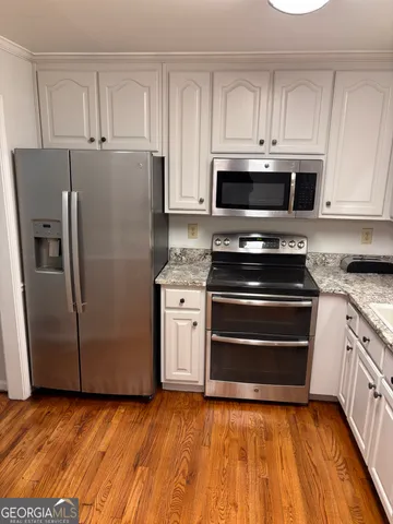 a kitchen with granite countertop a refrigerator stove and white cabinets