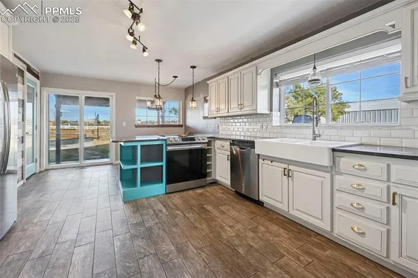 a kitchen with stainless steel appliances granite countertop a stove a sink dishwasher and white cabinets with wooden floor