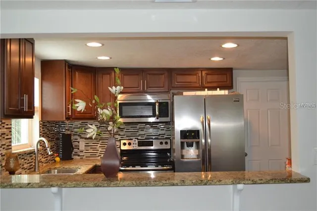 a kitchen with stainless steel appliances granite countertop a refrigerator a stove and a sink with wooden cabinets