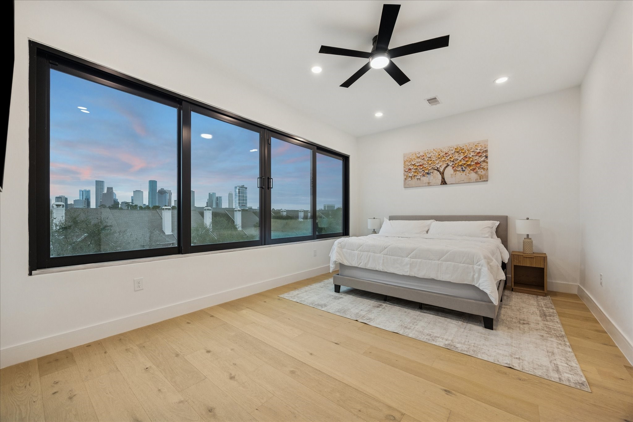809 Memorial Heights Drive Houston, TX 77007 - Photo 5 of 32 Spacious primary suite featuring wide-plank wood flooring and expansive windows showcasing stunning Houston skyline views.