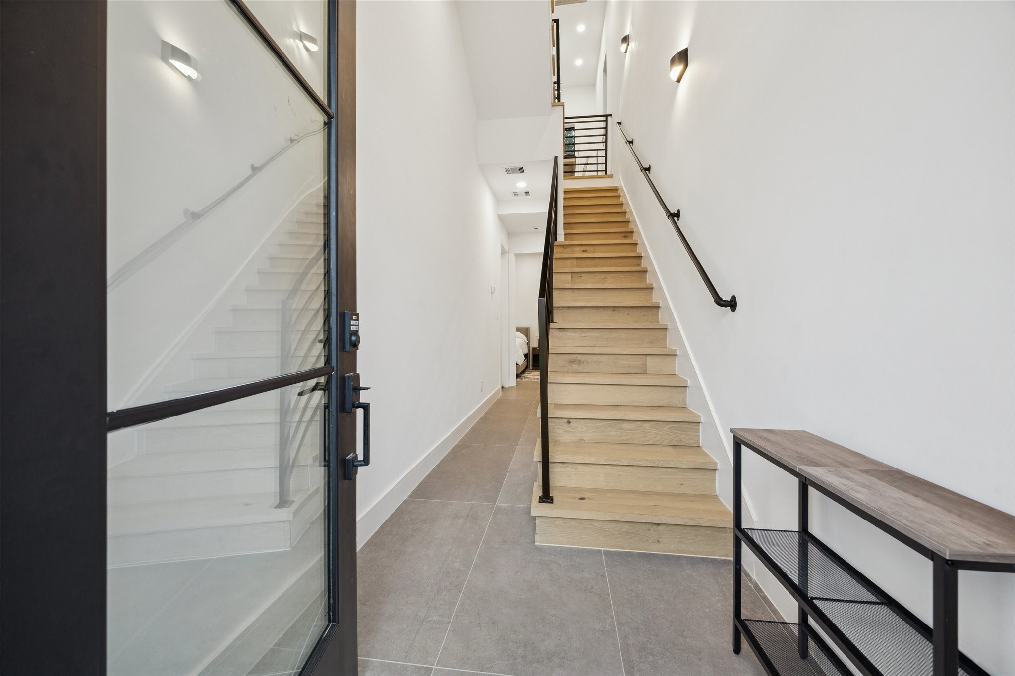 809 Memorial Heights Drive Houston, TX 77007 - Photo 7 of 32 Clean, modern foyer featuring a striking glass-front entry, oversized tile flooring, and an elegant staircase with modern railing details and warm wood accents.