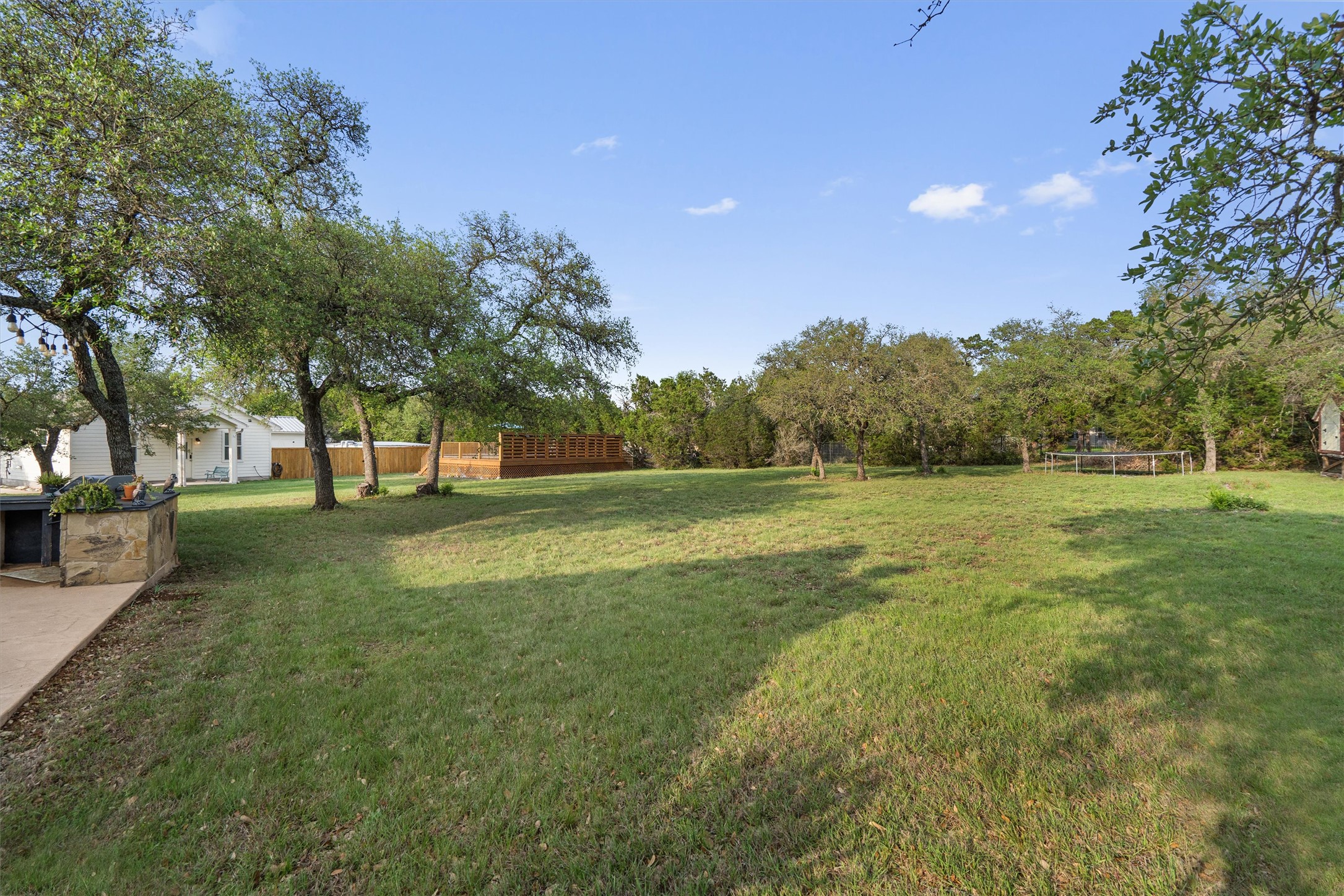 13105 Rooster Springs Road Austin, TX 78737 - Photo 25 of 38 Expansive outdoor living area with a large lawn and mature trees, featuring a stone outdoor kitchen with a grill