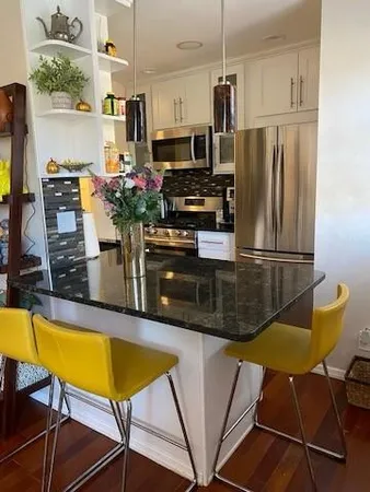 a kitchen with stainless steel appliances granite countertop a refrigerator a stove a sink a dining table and chairs with wooden floor